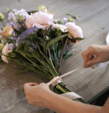 Händer som binder ett band runt en bukett med blommor på ett bord.