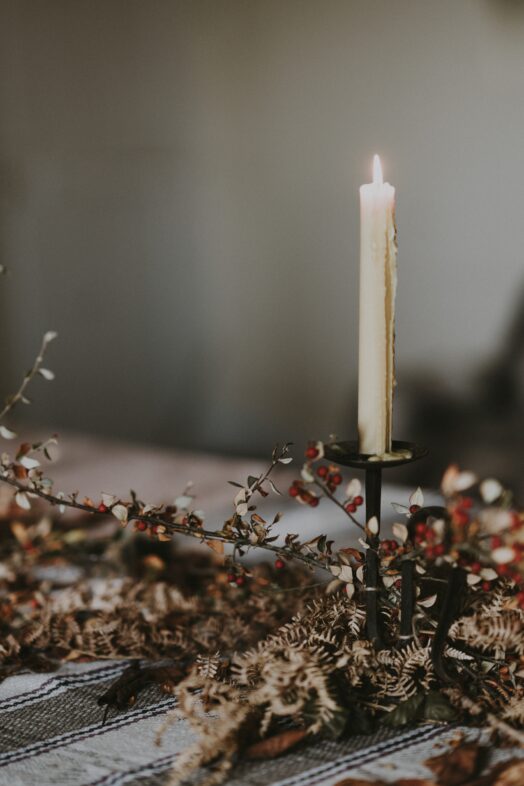 Ett ensamt ljus brinner på ett bord dekorerat med torkade blommor.