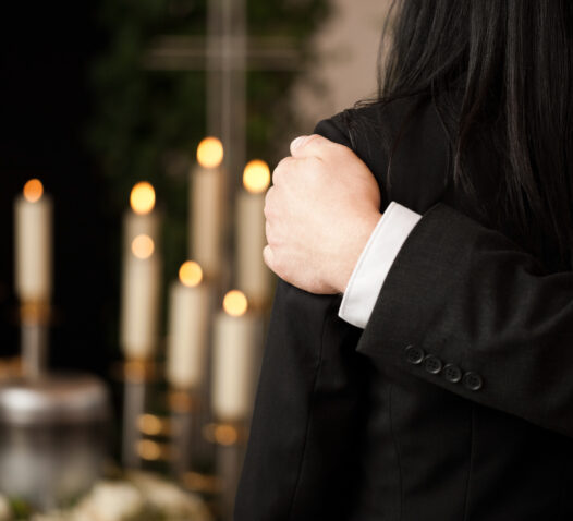 Någon i en svart kostym håller om en annan person framför tända ljus.