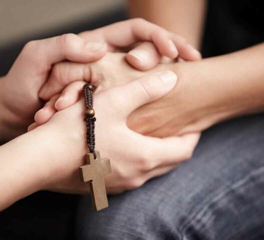 Två personer håller varandras händer, den ena med ett radband med ett träkors.